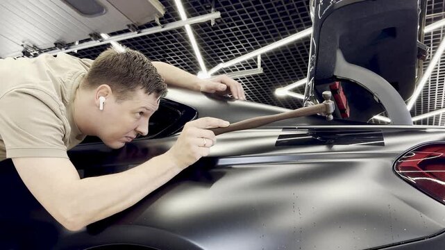PDR. Paintless Car Dent Repair. Process of paintless dent repair on car body. The mechanic at the auto shop with tools to repair dents in car body. Body repair. A specialist repairs a dent on the car.