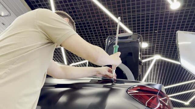 PDR. Paintless Car Dent Repair. Process of paintless dent repair on car body. The mechanic at the auto shop with tools to repair dents in car body. Body repair. A specialist repairs a dent on the car.