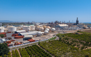 Obraz premium Wide view of large petrochemical refinery complex featuring spherical pressure vessels, storage tanks and industrial infrastructure extending toward Mediterranean port coastline, Spain
