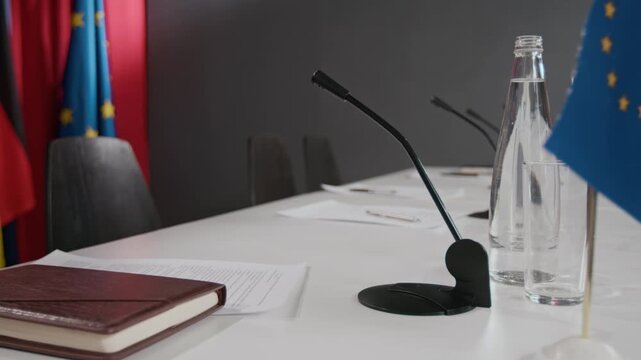 Conference table with microphones, notebook, and European Union flags empty before political summit. Suitable for international relations news and diplomatic press releases close up, side view