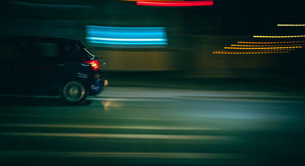 Fototapeta premium Dark car drives quickly along a city road at night, creating light trails and motion blur