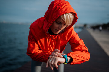 Fit woman setting smartwatch before running on seaside promenade. © Halfpoint