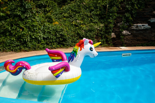 Unicorn pool float in blue water background, inflatable swim tube. Pool party, summer holidays, beach vacation. Fantasy swim ring for summer pool trip. Copyplace, place for text