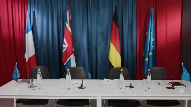 Empty international conference table standing ready with microphones, water bottles, and European flags. Footage is ideal for political news broadcasts and global summit reports, wide angle