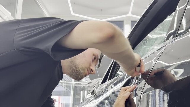 A car wrapping specialist applies a polyurethane film to the car. Detailer smoothes PPF. Car wrapping, detailing, tuning and styling. PPF protective film against chips and scratches. 