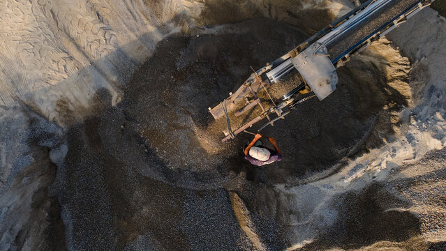 Aerial view of industrial sand quarry operations at Babakan with a conveyor belt pouring gravel onto a pile and a worker standing nearby in Karanglewas, Central Java, Indonesia.