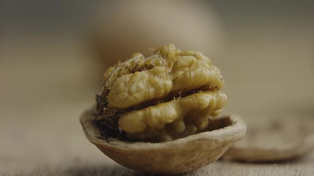 Close-up of a hand cracking open a walnut shell, revealing the soft, edible nut inside, with a blurred background of wooden surface and additional walnuts