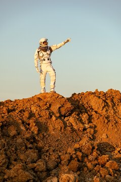 Astronaut stands on Martian surface pointing towards horizon during exploration in daylight