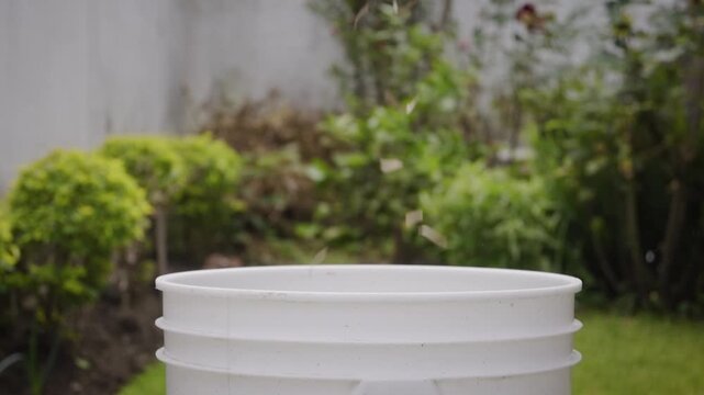Still image of cardboard shavings falling into a compost bin in a garden