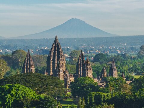 Aerial view of Prambanan Temple with its stone spires rising above lush green trees and Mount Merapi in the background Kecamatan Prambanan, Daerah Istimewa Yogyakarta, Indonesia.