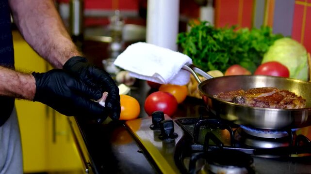 Chef in black gloves seasons, sears and bastes a ribeye steak with garlic and butter on a stainless steel pan. Complete medium rare steak recipe from preparation to slicing and serving.