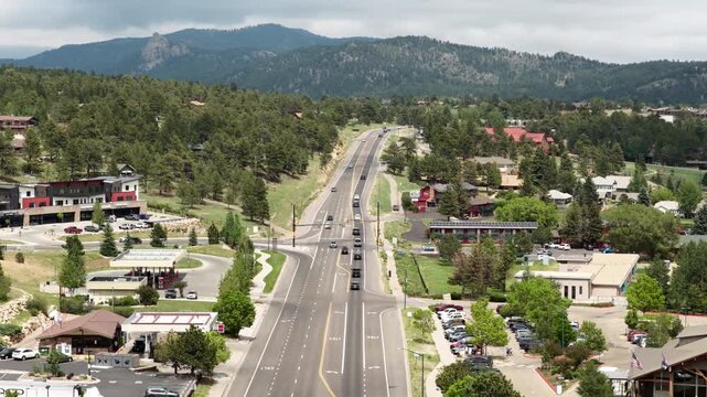 Aerial of highway 36 through small town Estes Park Colorado sunny summer day with commercial buildings lining the streets and dense forested mountains