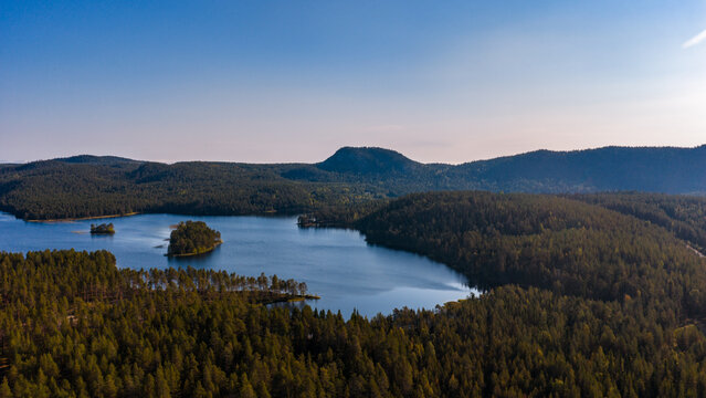 Aerial view of the Konttainen fell surrounded by dense pine forests and a calm lake under a clear blue sky in Kuusamo, North Ostrobothnia, Finland.