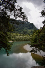 Obraz premium Alpsee Lake Surrounded by Forested Mountains Under a Cloudy Sky