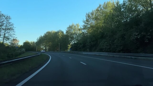 Amsterdam Netherlands highway, Sunlit motorway curving through trees toward underpass