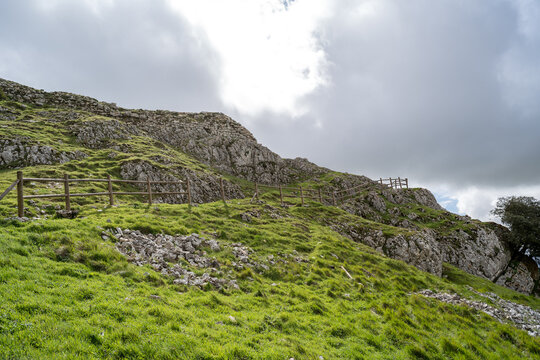 Wooden fence on a grassy slope leading to rocky hills of Monasterio de Rodilla castle, Spain