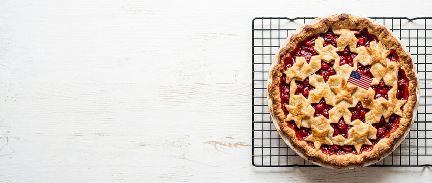 Cherry pie with star shaped crust and miniature American flag. Traditional homemade dessert for Independence Day celebration. American patriotic holiday food on wooden white background.