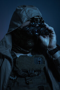 Man in civilian hooded jacket using bridged dual thermal and white phosphor night vision monocular system in dark conditions