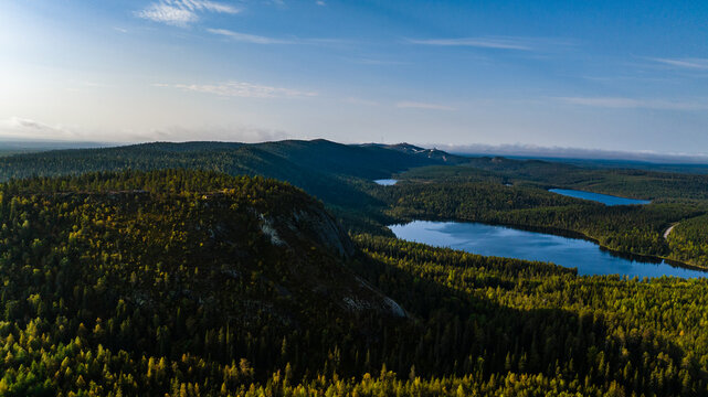Aerial view of the Konttainen hill with its rocky cliff overlooking dense forests and blue lakes under a clear sky in Kuusamo, North Ostrobothnia, Finland.