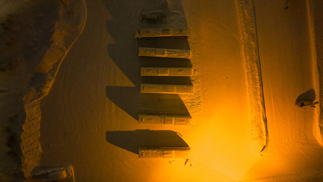 Aerial view of buses parked in a row at Luosto, covered in snow and illuminated by artificial orange light at night in Sodankyla, Lapland, Finland.