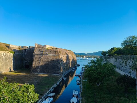 Ancient Venetian New Fortress massive stone walls with moat canal and moored fishing boats in golden morning light, Corfu Old Town, Greece, June 5 2026