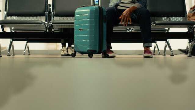 Multicultural group of passengers waiting before interstate coach departure, inside regional bus hub, travelers group with carry-on luggage checking departure board, long-haul relocation travel.