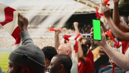 Obraz premium Vertical green screen mockup held by supporter during live football match, surrounded by cheering soccer fans and packed stadium stands, Crowd excitement.