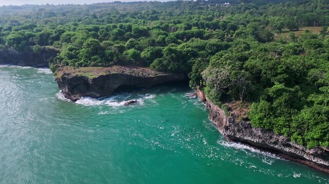 Coastal arches and limestone formations. Waves surge through caves beside rugged cliffs. Green cliffs overlook sheltered inlets with textured shoreline patterns,Bali