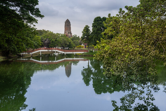 A serene view of the ancient Ayutthaya Historical Park ruins in Ayutthaya, Thailand, reflected in the calm waters of a pond on an overcast day.