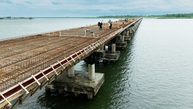 Aerial view of a bridge under construction with workers on the deck and rebar structures over calm water in Rivers State, Nigeria.