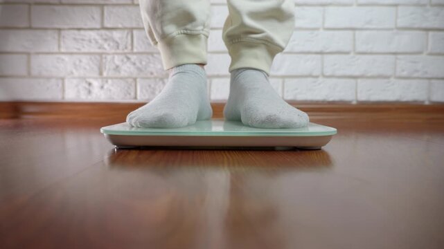 Measuring weight on electronic scales. Female feet in gray socks stepping onto a modern digital weight scale, meticulously checking her body weight at home for health monitoring and fitness tracking