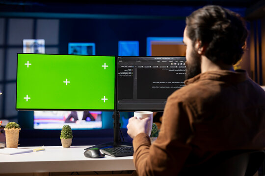 Programmer drinking hot beverage and using green screen PC for futureproofing company network from downtimes and unexpected system failures. Admin with coffee mug in front of mockup computer.