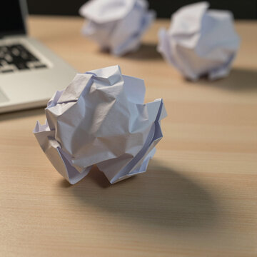 crumpled paper balls on wooden desk near laptop, reflecting creativity and frustration