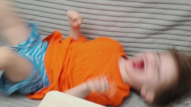 A cute little boy, 2-3 years old, is lounging on the couch, laughing, playing, kicking, misbehaving, and disobeying his mother. Child-rearing challenges