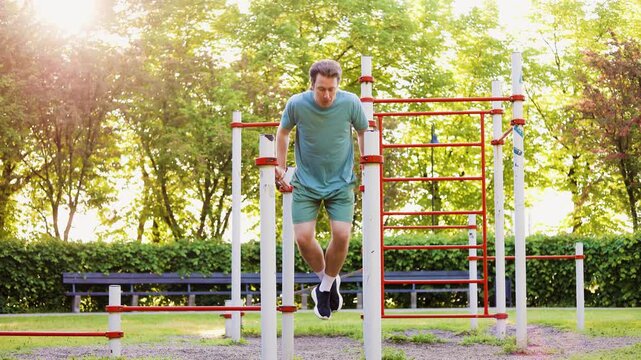 A fit man doing tricep dips at an outdoor gym park. Healthy lifestyle, calisthenics workout, and strength fitness exercise in the sunny summer nature. High quality 4k footage