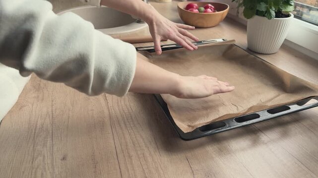 Straight parchment paper keeps curling back while being placed on tray. Helpful visual for kitchen problem solving baking preparation and practical cooking instruction content.