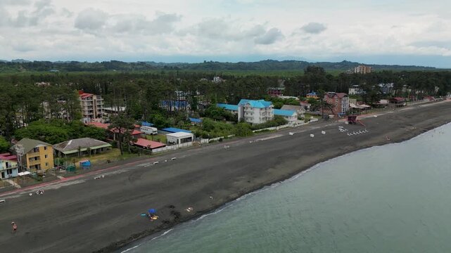 Drone view of the coastal road and resort area near Ureki Beach, Georgia, with the Black Sea shoreline, buildings and green hills in the background.