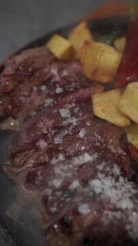 Delicious sliced beef ribeye steak cooking on a hot stone plate. Coarse salt is melting on the juicy meat served with potatoes and peppers