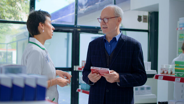 Aged man in chemist store asking pharmacist for medical opinion, needing treatment for cardiovascular issues, druggist helping Senior client choose best pharmaceutical pills for his affliction