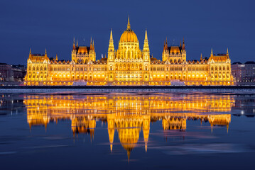 Naklejka premium Magnificent view of the illuminated Hungarian Parliament Building with gold reflection in the Danube river, Budapest