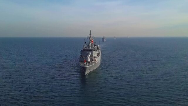 Aerial drone shot of a Turkish Navy guided-missile frigate leading a column of warships in a historic naval parade formation through the Bosphorus Strait.