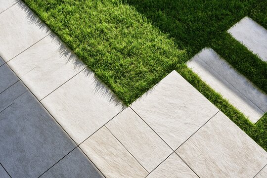 Patch of green lawn on modern tiled patio walkway corner