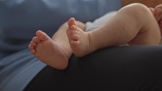 Newborn boy feet being gently touched and played with by adult hand on lap in home; parental bonding tenderness.