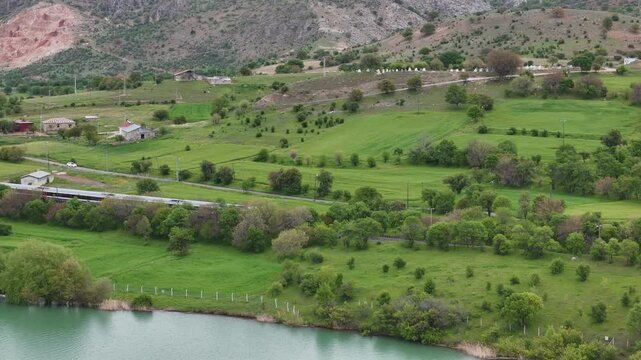 Aerial view of a passenger train traveling through a lush green landscape next to a peaceful river.