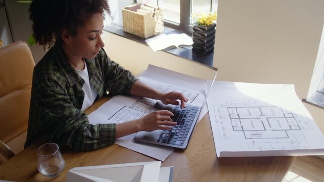 African American designer with drafts types on laptop in office
