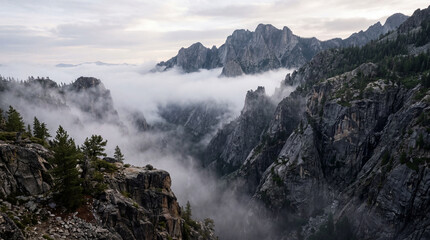 Obraz premium Deep mountain ravine is enveloped in thick morning fog showing jagged granite cliffs landscape view.