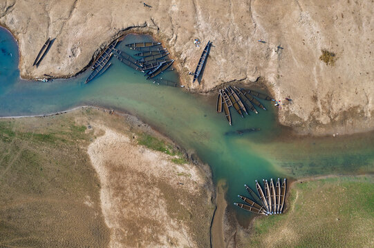 Aerial view of traditional wooden boats moored along the sandy banks of a turquoise river in Sylhet, Sylhet Division, Bangladesh.