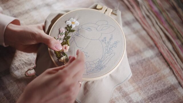 Experienced Craftswoman Carefully Sews Floral And Rabbit Designs Onto Fabric In Wooden Hoop . Media
