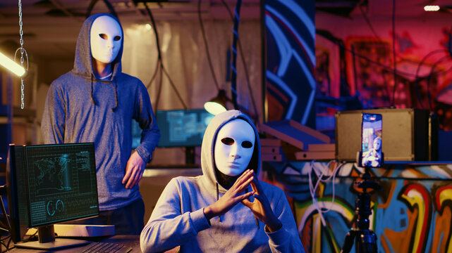 Social justice warriors wearing anonymous masks filming video threatening country government to steal military secrets, being upset about policies putting citizens at risk.