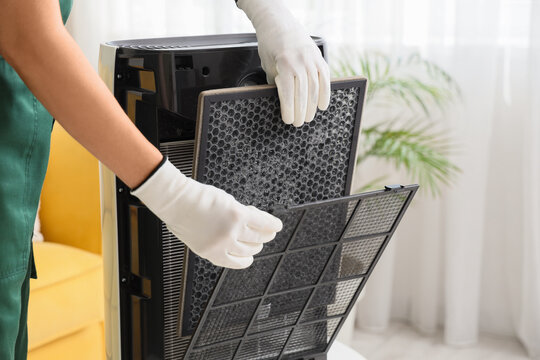 Young female worker changing filter in modern air purifier at home, closeup